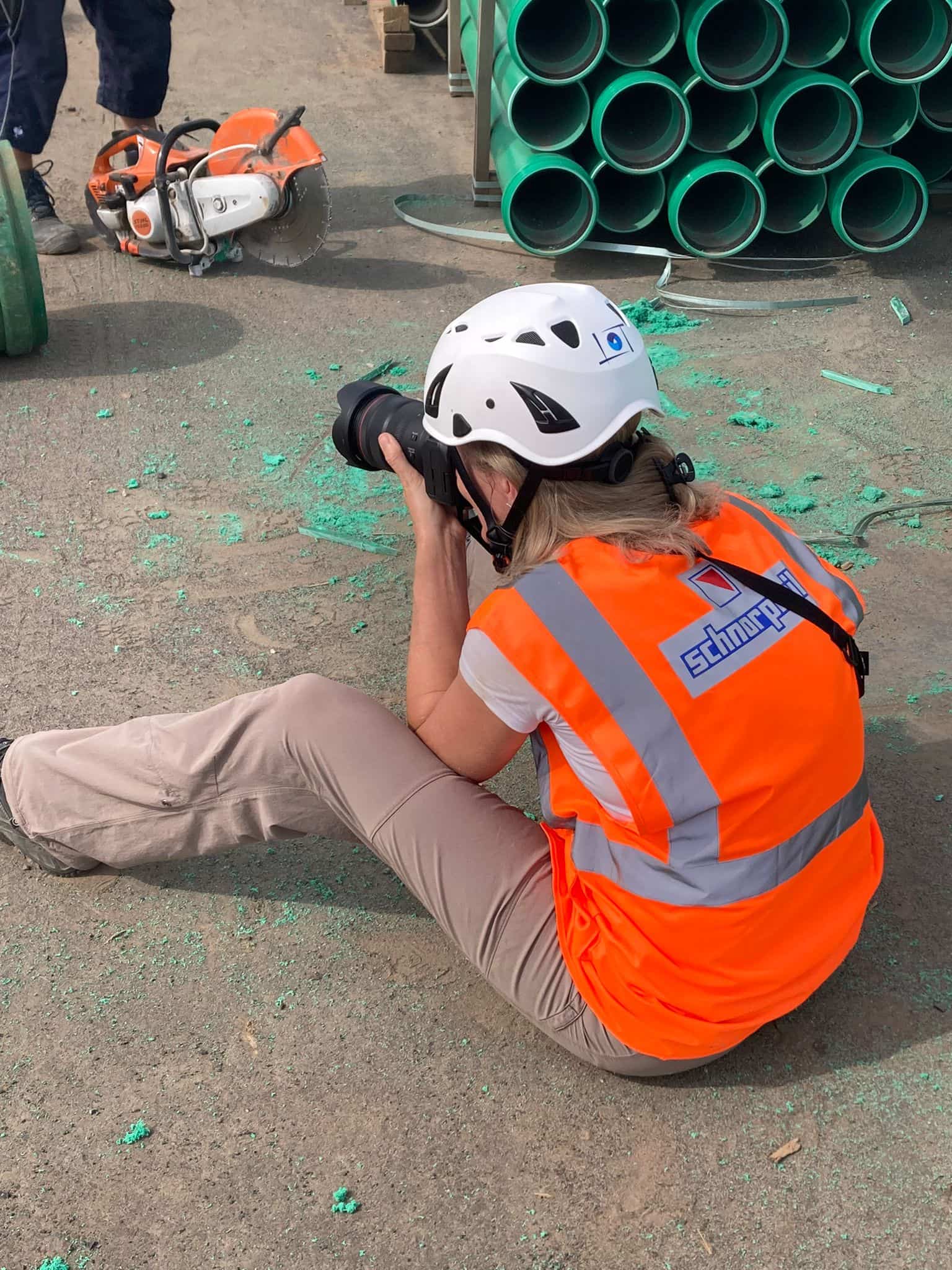 Britta Hilpert Baufotografin sitzend beim Fotografieren mit Sicherheitshelm und Warnweste.