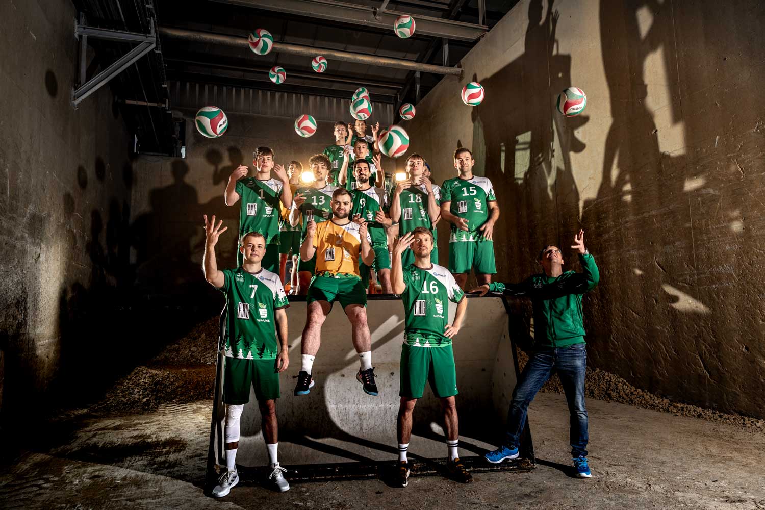 Die Herren-Mannschaft Westerwald-Volleys um und an einem großen Radlader platziert innerhalb der Tonfabrik Blumentopf Spang werfen gerade Bälle in die Luft.